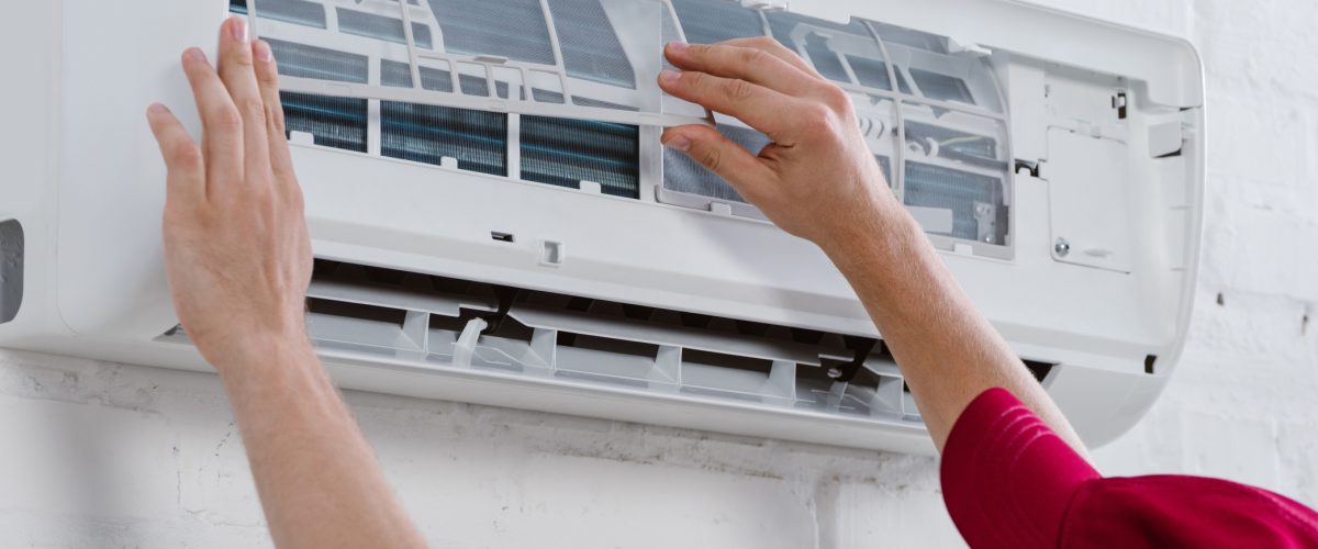 close-up shot of professional repairman changing filter for air conditioner hanging on white brick
